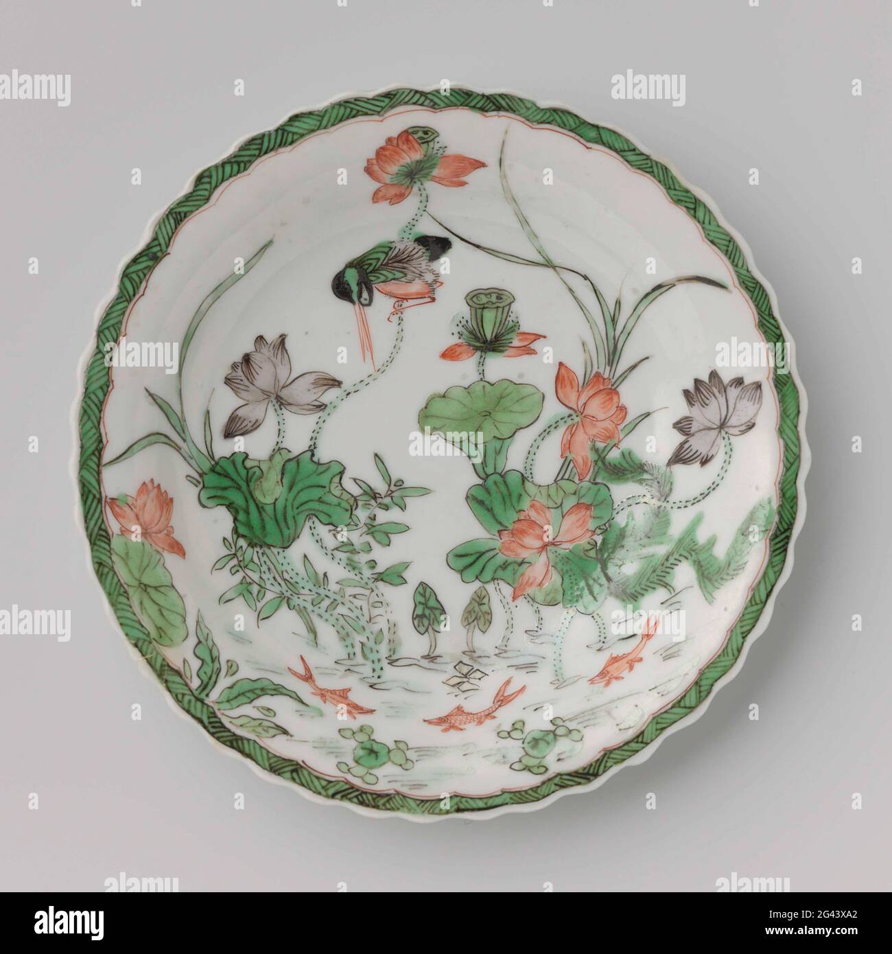 Soucoupe avec une livre, plantes de Lotus, poisson et oiseaux. Plat de porcelaine aux bords lobés, peint en bleu sous-glaçure et sur le rouge, le vert, le jaune, l'aubergine et le noir. Sur le plateau du plat un étang avec des plantes de lotus, trois poissons et un kingfisher, le bord avec le travail en zigzag; trois branches de fleurs à l'arrière. Plat marqué sur le fond avec un repère de joint dans un double cercle. Famille verte. Banque D'Images