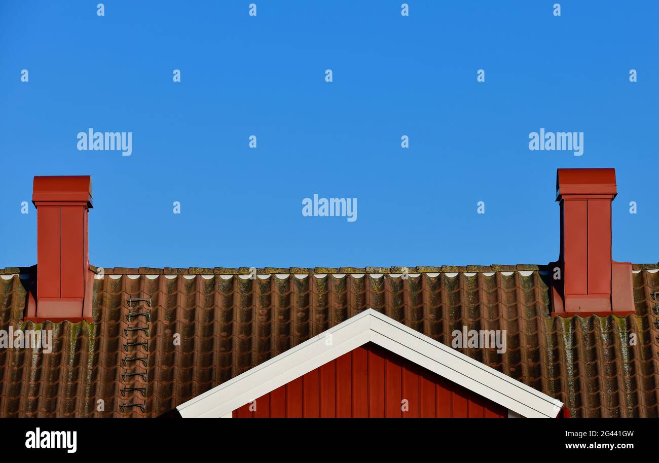 Vue d'une maison suédoise rouge contre un ciel bleu avec 2 cheminées, Grimsholmen, Halland, Suède Banque D'Images