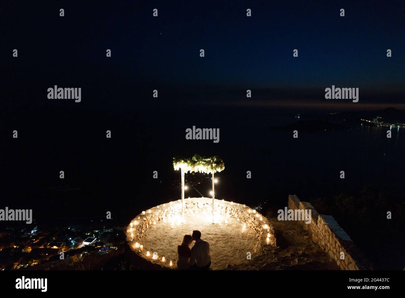 Silhouettes de la mariée et du marié qui s'asseyent près la zone éclairée et l'arche de mariage au bord de la mer la nuit Banque D'Images