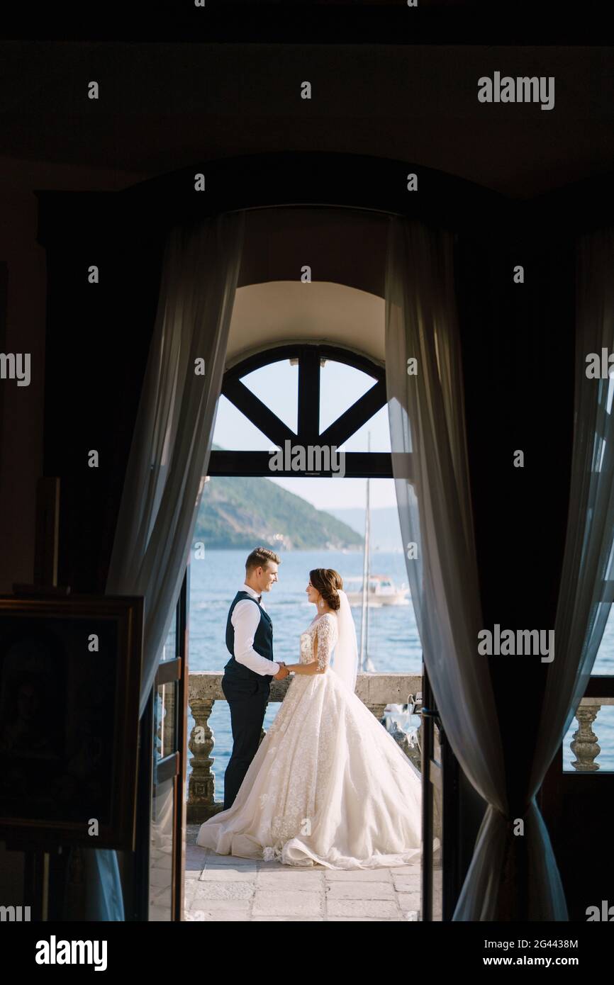 La mariée et le marié sont debout sur le balcon de l'hôtel donnant sur la mer, un regard à travers la vieille fenêtre ouverte. Les arts plastiques avec Banque D'Images