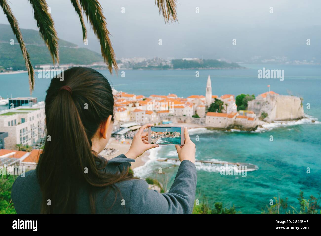 Une fille aux cheveux foncés prend des photos de la ville de Budva de loin sur smartphone Banque D'Images