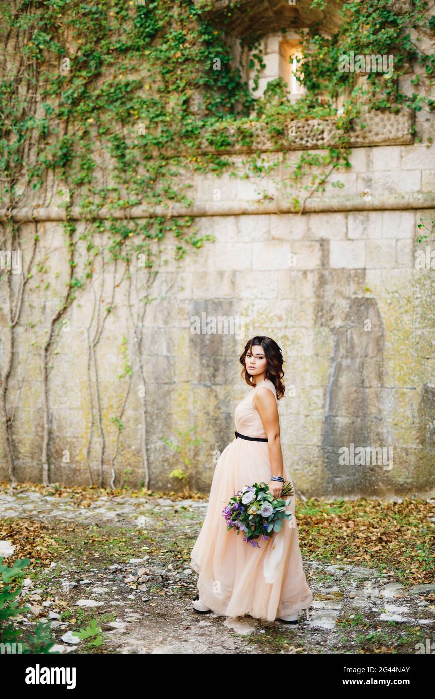 Belle mariée dans une robe pastel marche avec un luxueux bouquet de fleurs sur le mur Banque D'Images