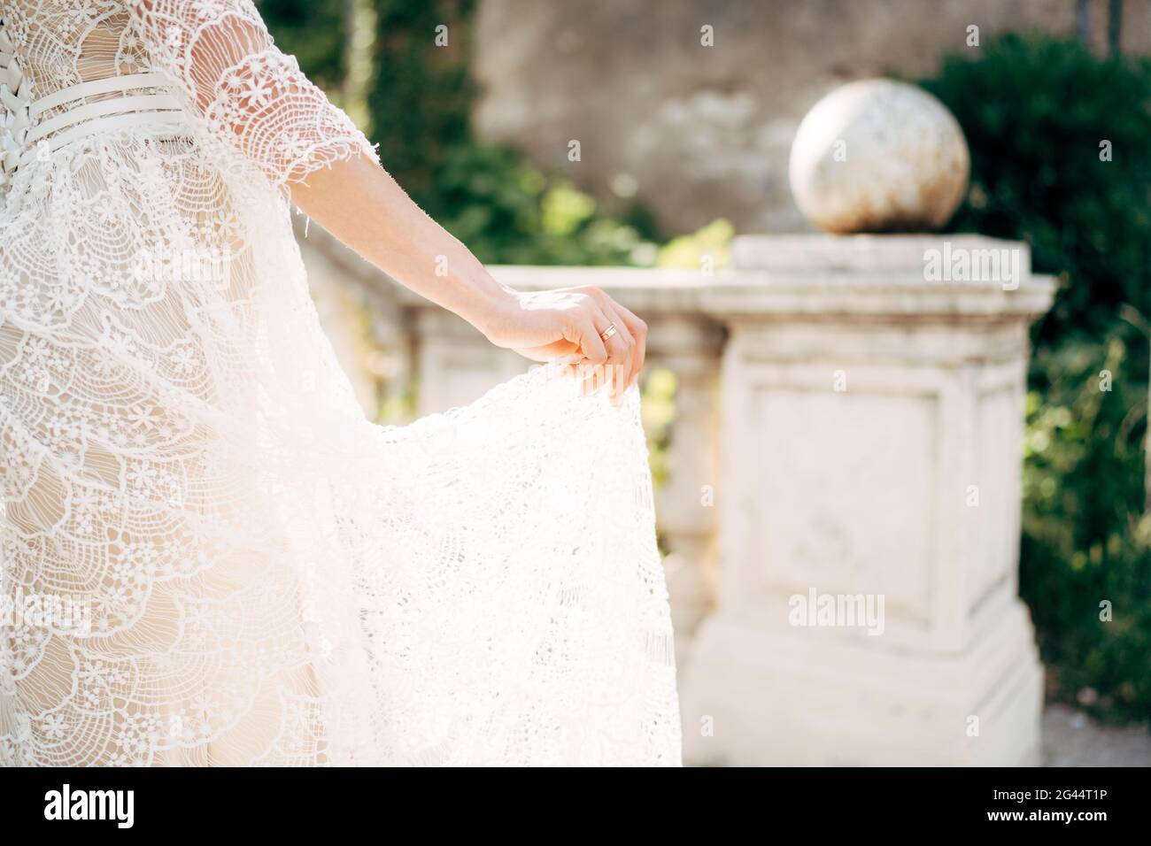 Mariée tient avec ses doigts le plancher d'un blanc robe de mariage en dentelle sur le fond des colonnes dans le jardin Banque D'Images