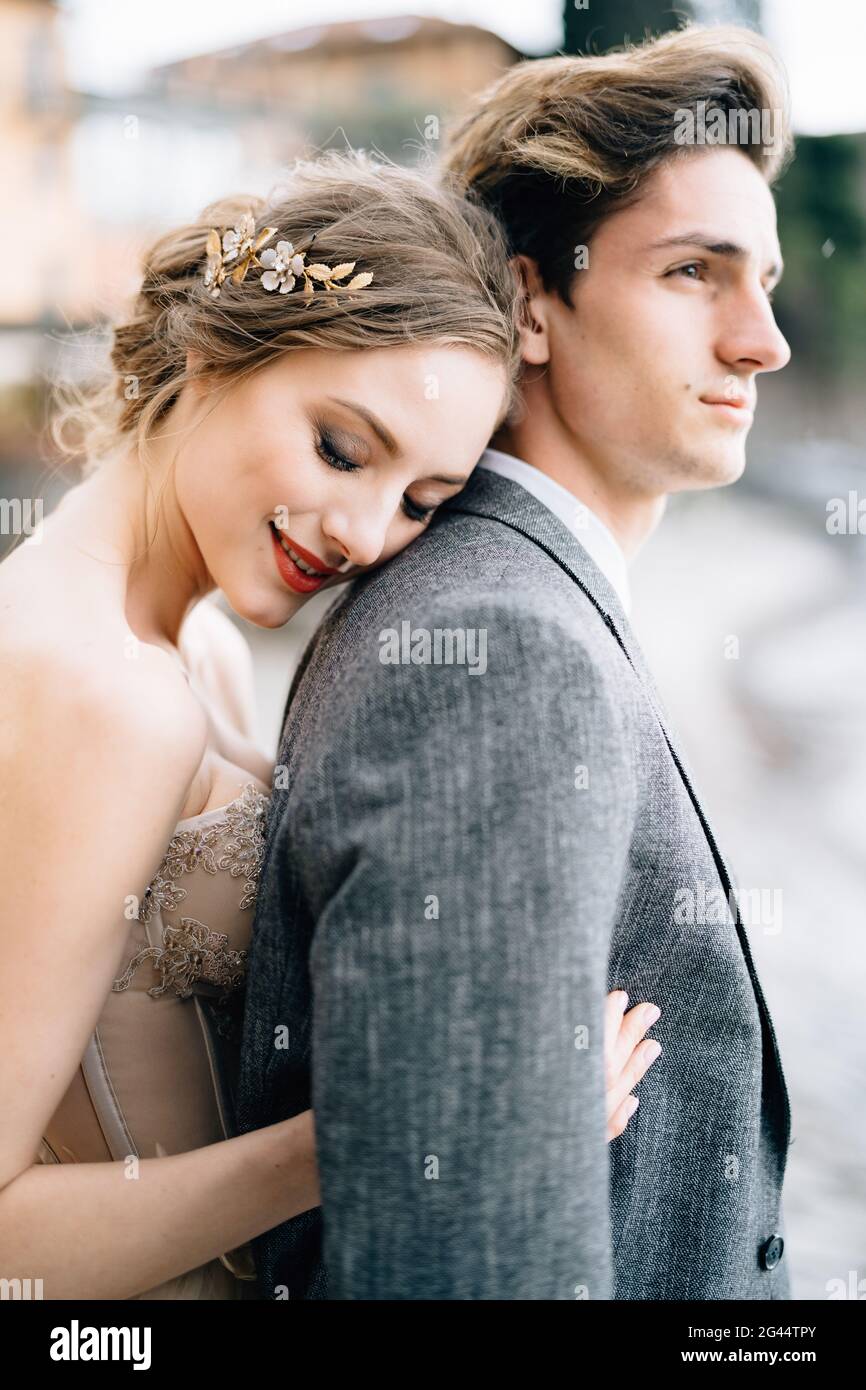 Une mariée souriante encadre le marié de derrière tout en se tenant sur la promenade du lac de Côme. Demi-portrait Banque D'Images