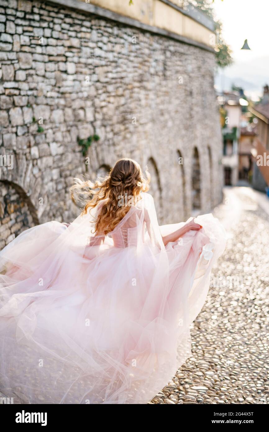 Mariée dans une robe flottant dans le vent court le long des pavés d'une vieille rue à Bergame, Italie. Vue arrière Banque D'Images