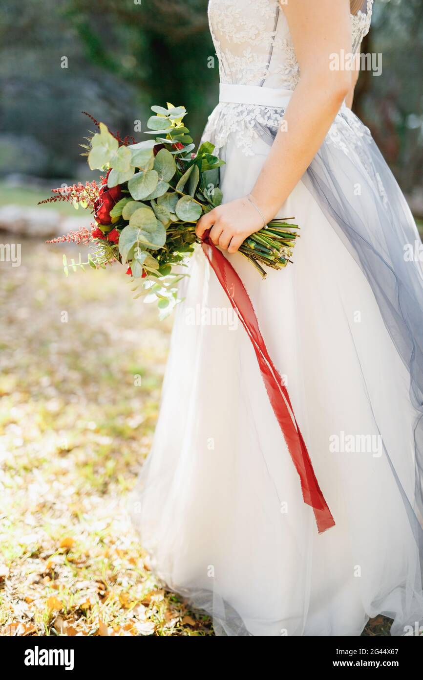 Une mariée dans une robe de mariage gris pâle tient un bouquet de pivoines  rouges, astilba, roses et eringium et rouge longs rubans, close-u Photo  Stock - Alamy