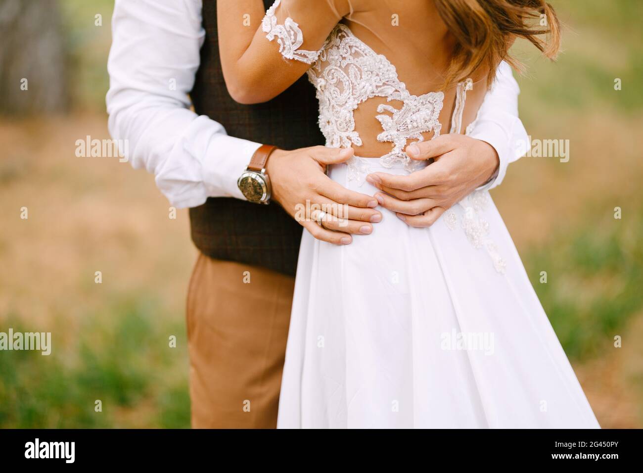 Le marié tient ses mains à la taille de la mariée dans une belle robe blanche brodée. Mariée se tient avec son dos tourné Banque D'Images