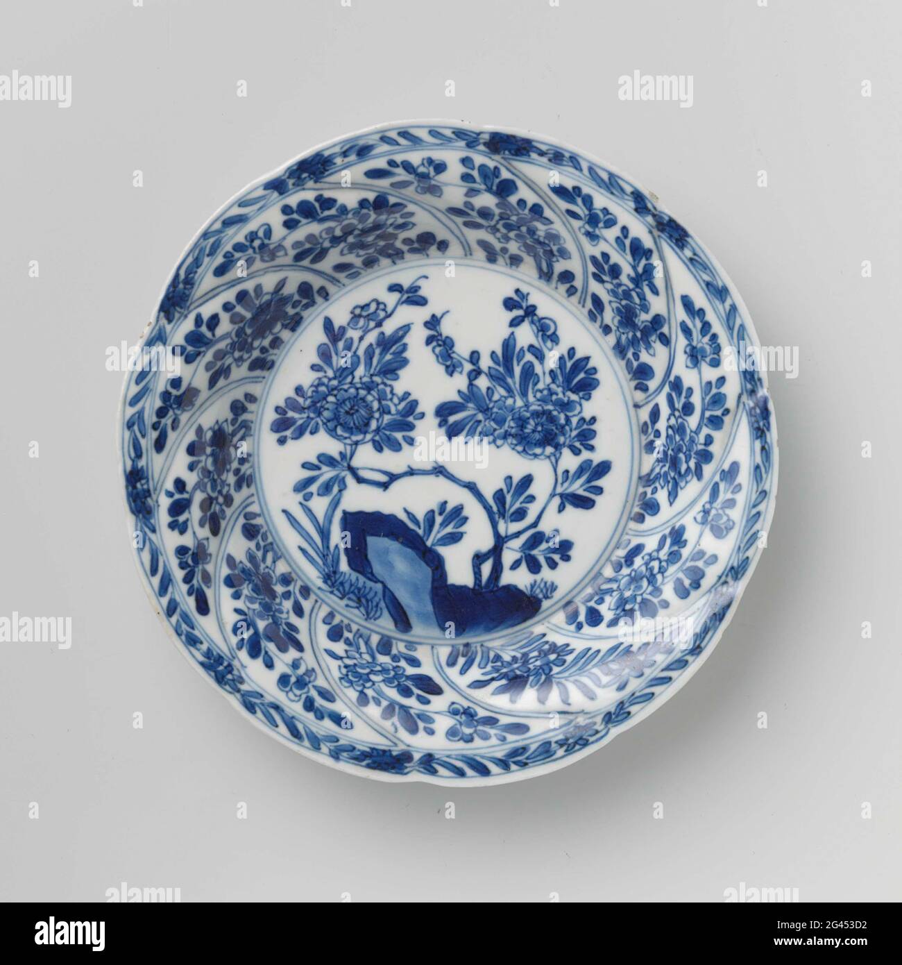 Soucoupe avec panneaux torsadés et sprays à fleurs. Plat en porcelaine à paroi ronde, modelé en dix boîtes, peint en bleu sous-glaçure. Sur l'appartement un rocher avec une branche de fleur et des plantes; une branche de fleur sur le mur dans chaque boîte; le bord avec une boisson de fleur; sur le dos aussi dans chaque boîte une branche de fleur. Le caractère chinois 'Fú' est marqué en bas dans un double cercle. Une puce dans le bord. Bleu blanc. Banque D'Images