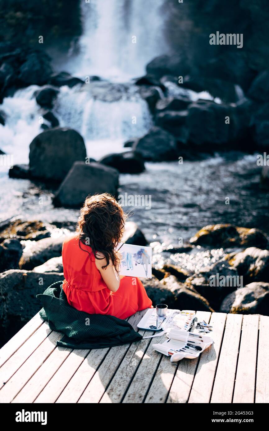 La jeune fille peint une photo de l'album avec des aquarelles. Près de la chute d'eau d'Ehsaraurfoss, de la rivière Ehsarau, du parc national de Thingvedlir Banque D'Images