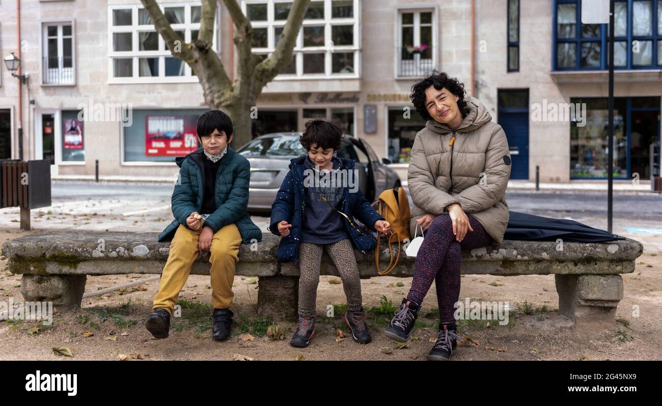 jeune mère assise avec ses deux fils de ses sur un banc de pierre dans un parc urbain Banque D'Images