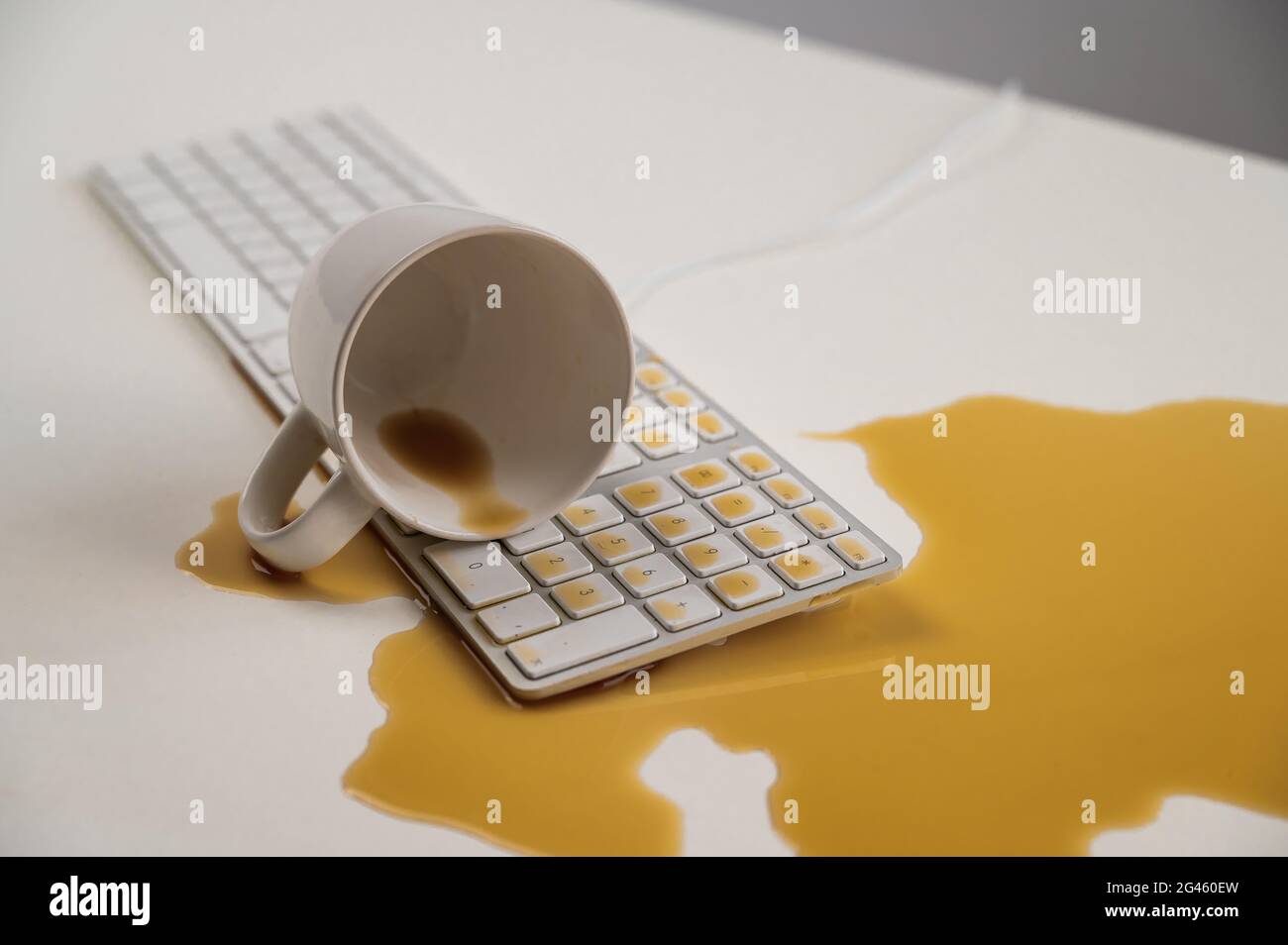 Tasse de café noir renversée sur le clavier de l'ordinateur sur la table blanche. Banque D'Images Tasse de café noir renversée sur le clavier de l'ordinateur sur la table blanche. Banque D'Images