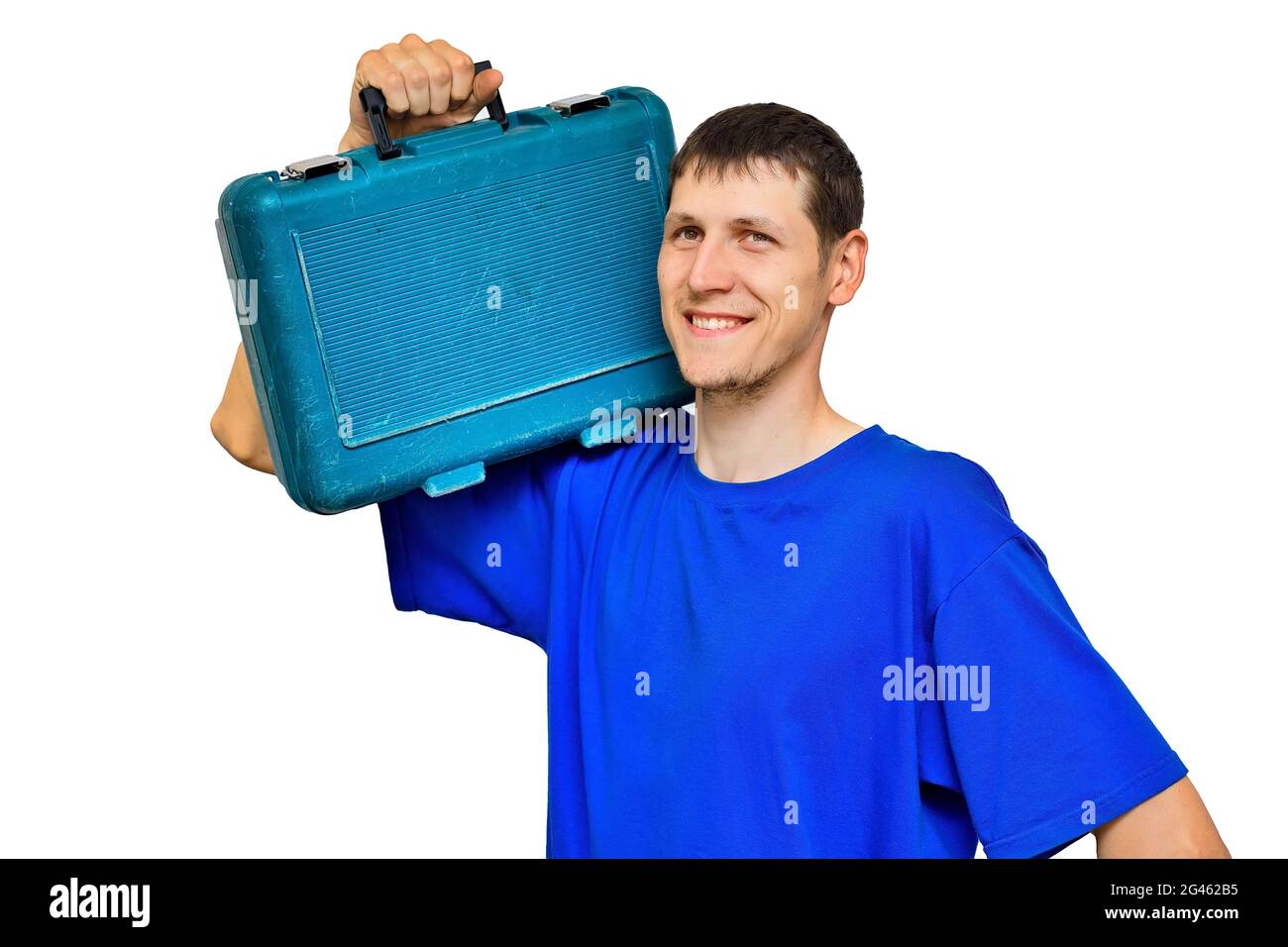 Un jeune travailleur en T-shirt bleu tient une valise avec des outils sur son épaule et sourit. Portrait isolé sur fond blanc. Réparations urgentes sur appel. Banque D'Images