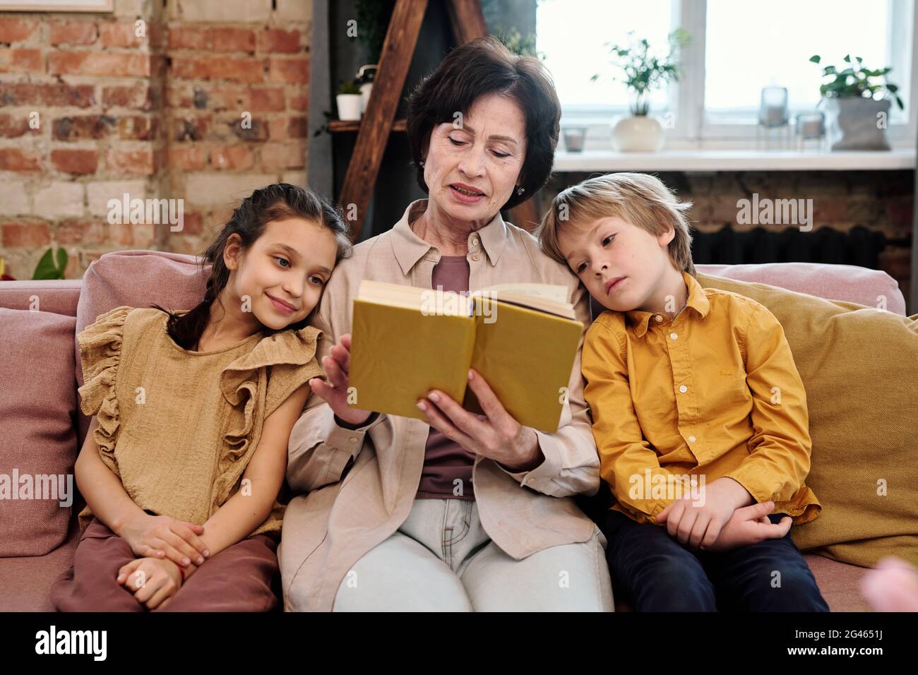 Livre de lecture de femme mûre avec ses petits-enfants dans la salle de séjour Banque D'Images