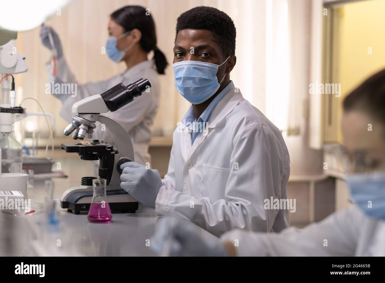 Jeune homme chimiste africain en casque de protection à l'aide d'un microscope Banque D'Images