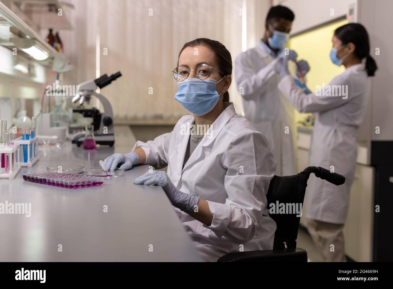 Jeune femme en vêtement de travail de protection assise sur le lieu de travail dans un laboratoire médical Banque D'Images
