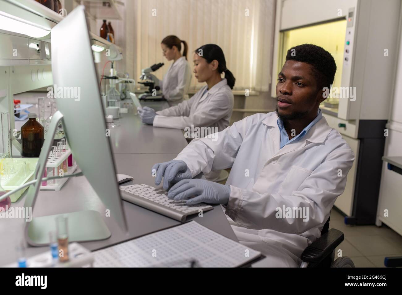 Jeune scientifique masculin en gants et en blanchon assis devant l'écran d'ordinateur en laboratoire Banque D'Images