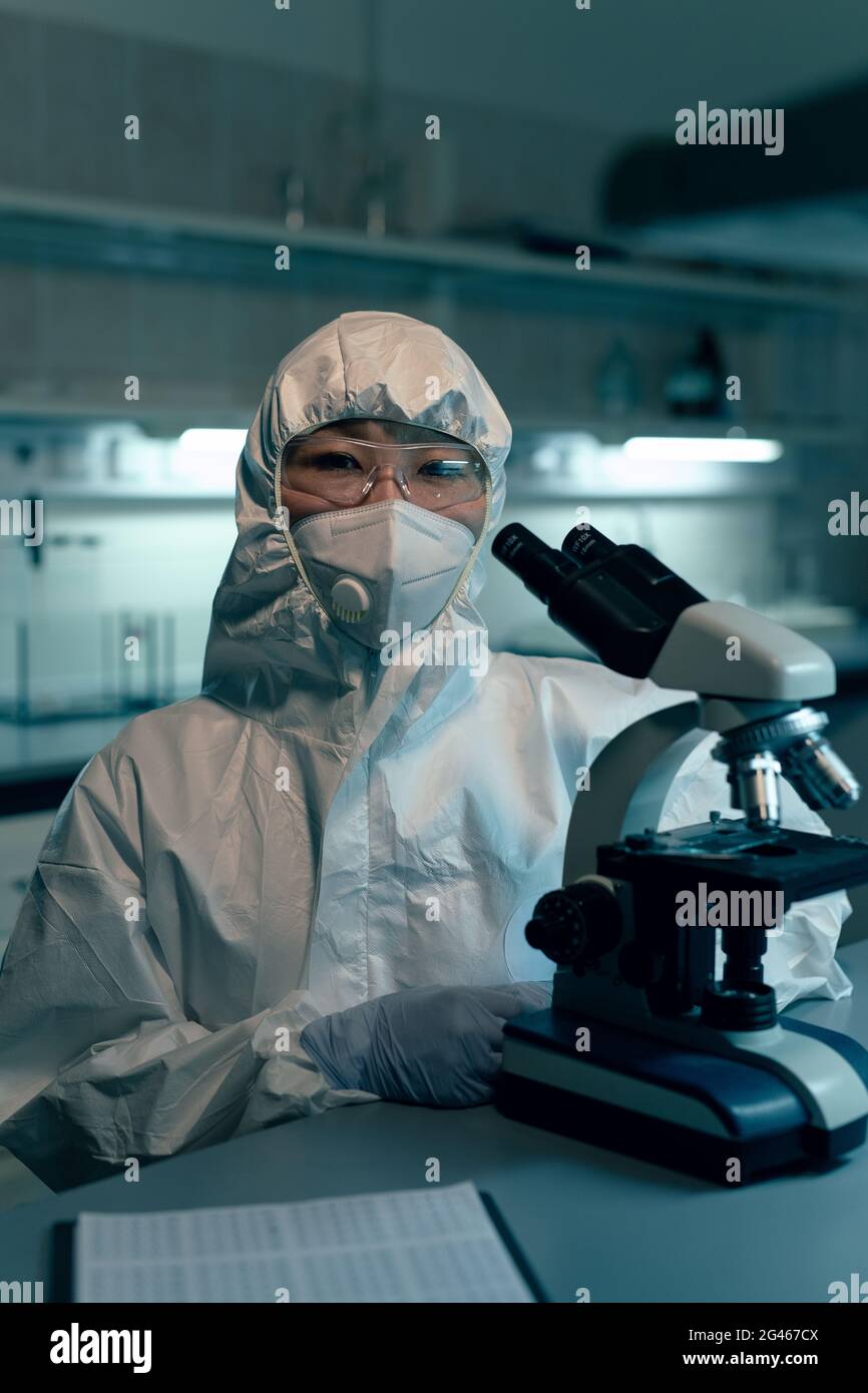 Femme scientifique en vêtements de travail de protection vous regardant par le lieu de travail en laboratoire Banque D'Images