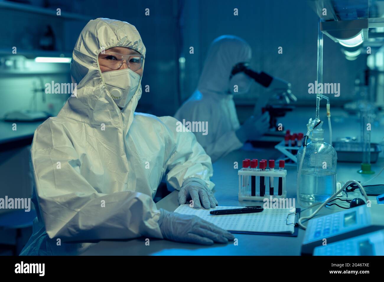 Jeune chercheuse dans des combinaisons et autres vêtements de travail de protection assis en laboratoire Banque D'Images