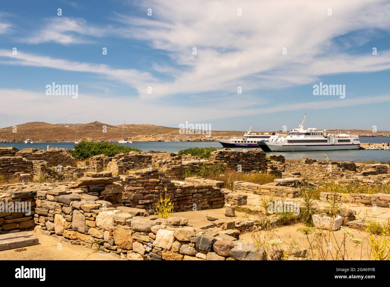 Vue sur une baie sur l'île de Delos, Grèce, avec des navires touristiques de Mykonos ancrés et des ruines et colonnes anciennes de la ville au premier plan. Banque D'Images