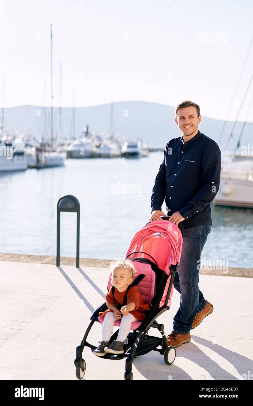 L'homme pousse sa fille dans une poussette rose un quai pour bateaux Banque D'Images