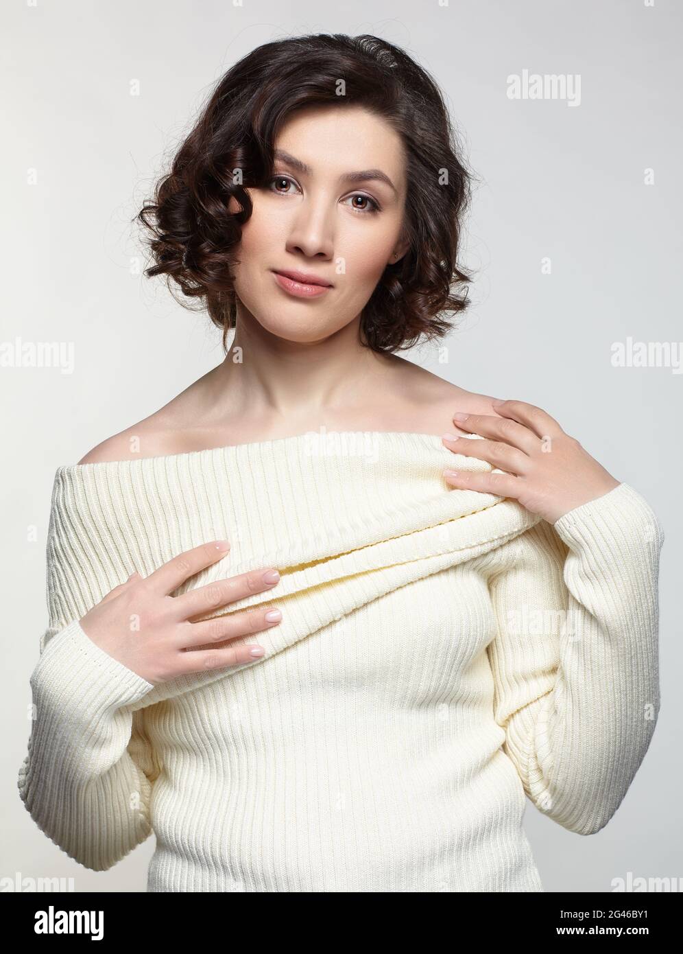 Brunette belle femme vêtue de grand chandail blanc en laine sur fond gris. Banque D'Images