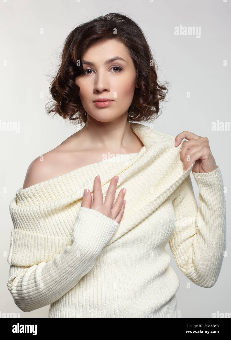 Brunette belle femme vêtue de grand chandail blanc en laine sur fond gris. Banque D'Images