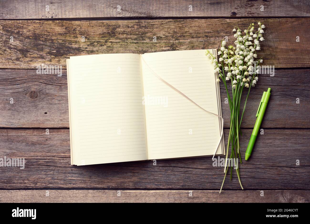 Carnet ouvert avec des feuilles blanches vierges et un bouquet de lys fleuris de la vallée sur une table en bois de planches grises Banque D'Images