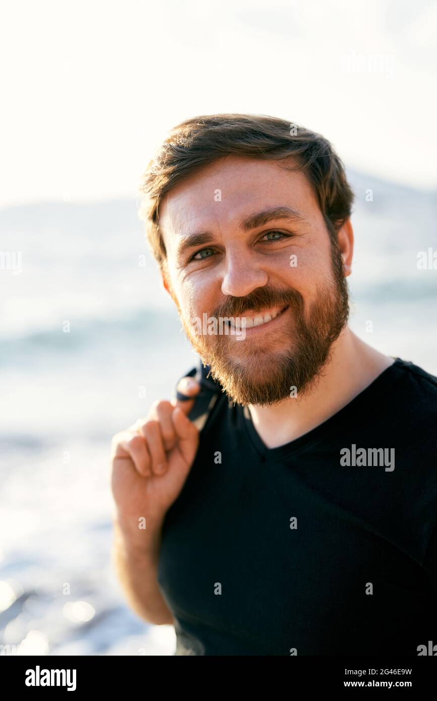 Homme souriant dans une veste en denim au-dessus de son épaule se tient contre le fond de la mer. Gros plan. Portrait Banque D'Images