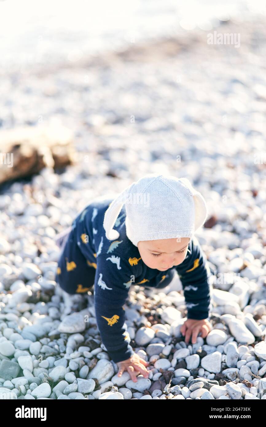 Un Petit Bebe Dans Une Combinaison Et Un Chapeau Rampent Le Long D Un Plage De Galets Sur Le Fond D Un Bois De Greve En Bois Photo Stock Alamy