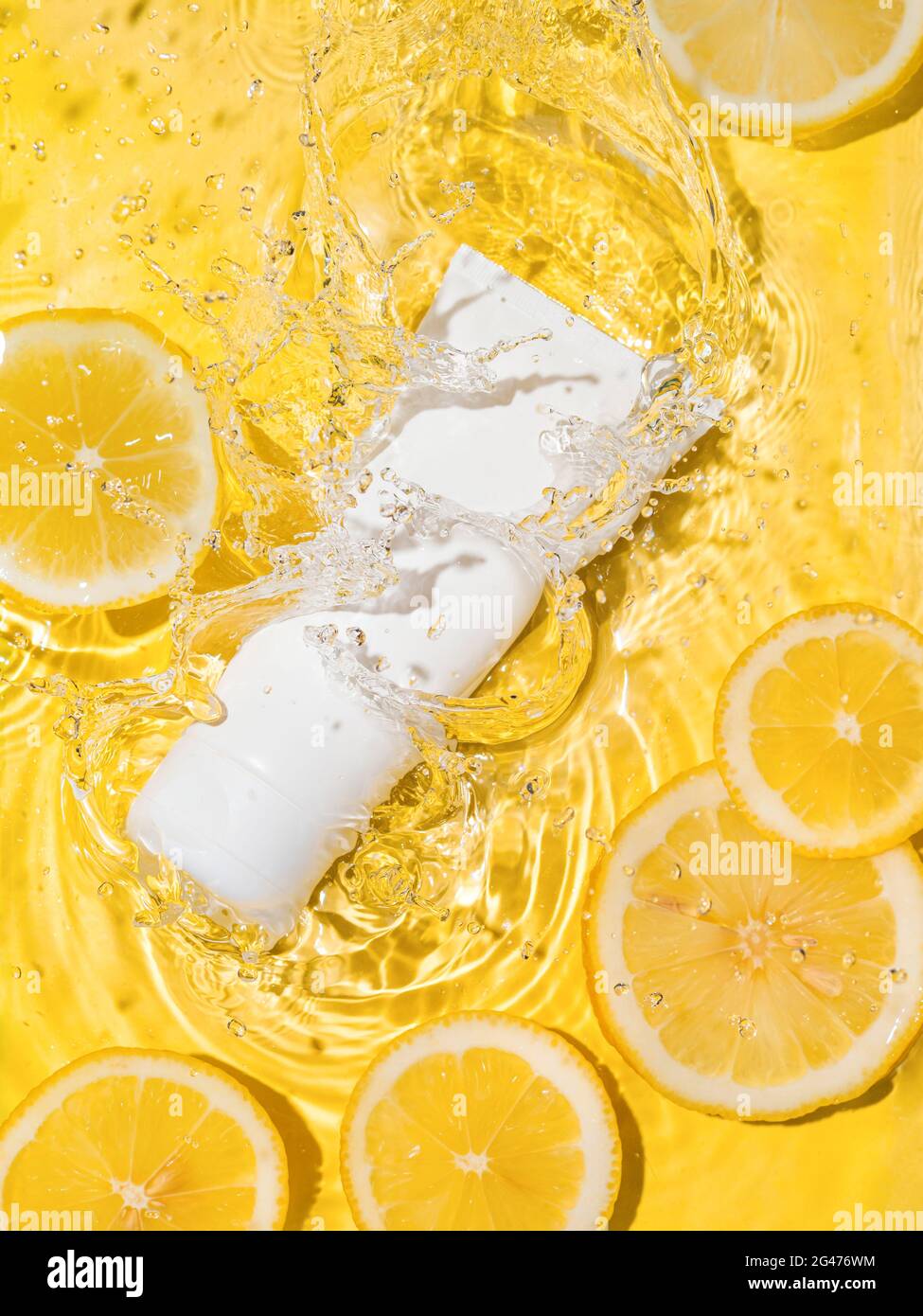 Tube cosmétique dans l'eau, tranches de citron, bg jaune Banque D'Images