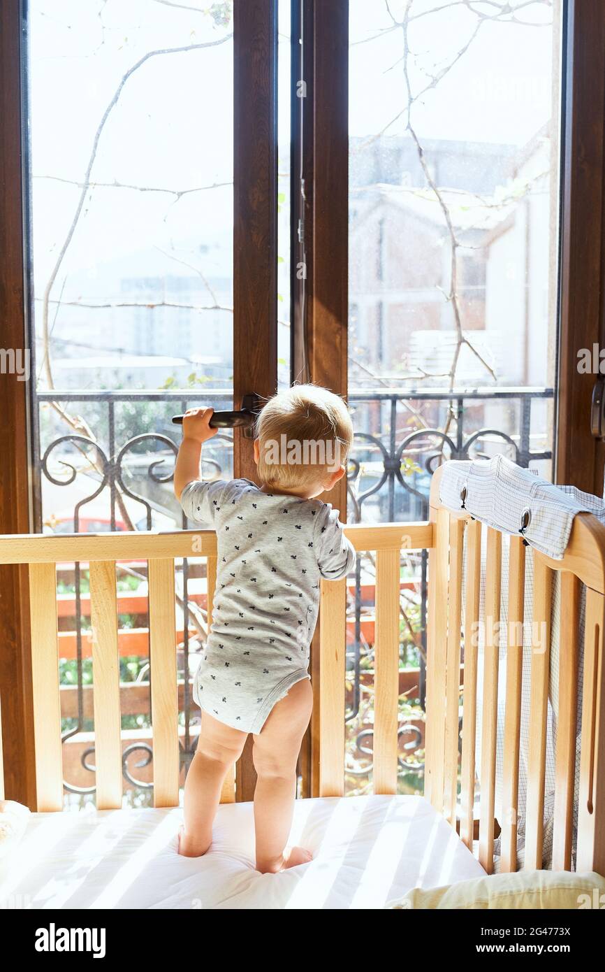 Un petit enfant ouvre la porte du balcon, debout dans un lit bébé en bois.  Vue arrière Photo Stock - Alamy