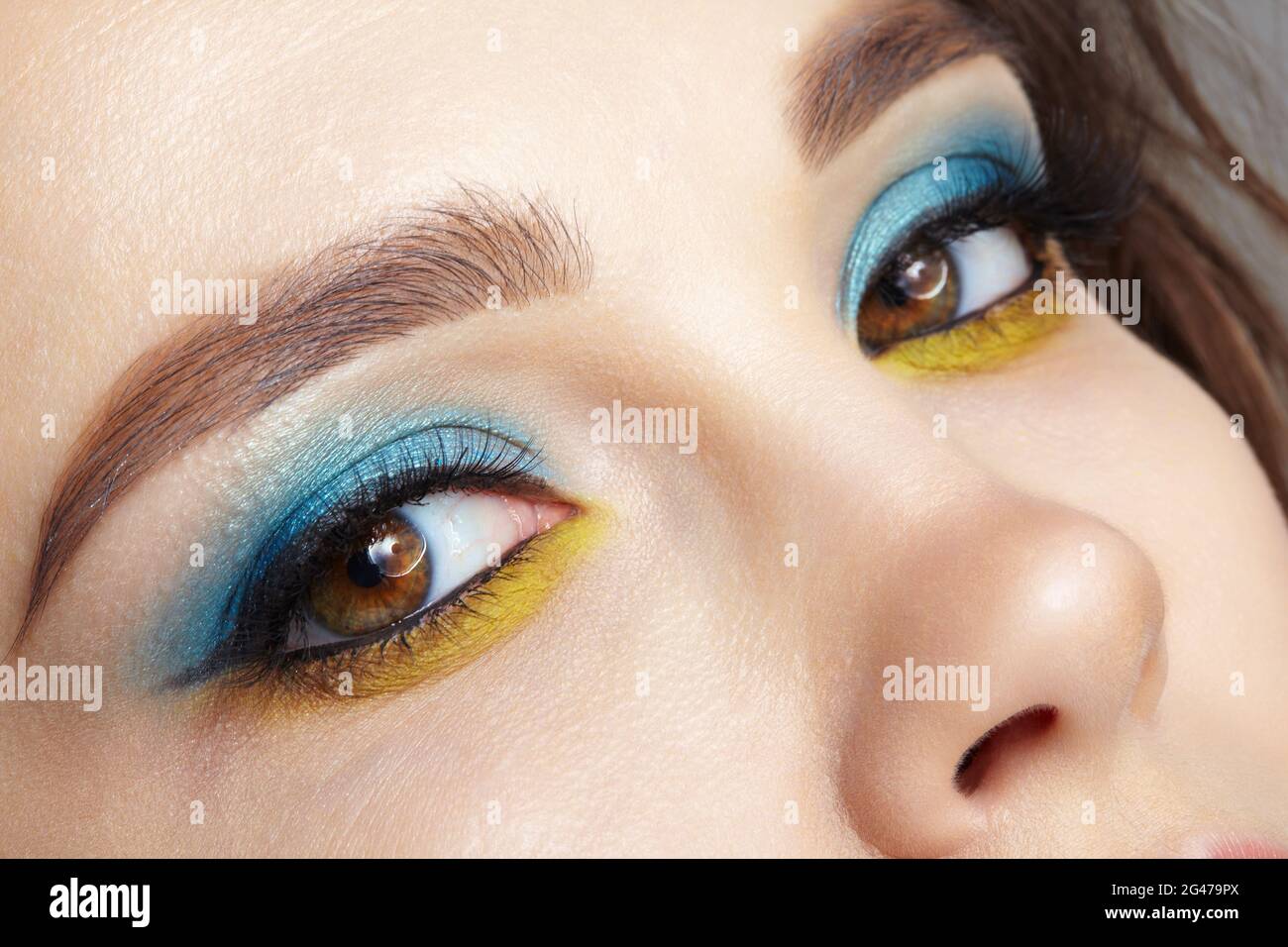 Gros plan sur le visage de la femme humaine avec doublure jaune et ombres à paupières bleues. Banque D'Images