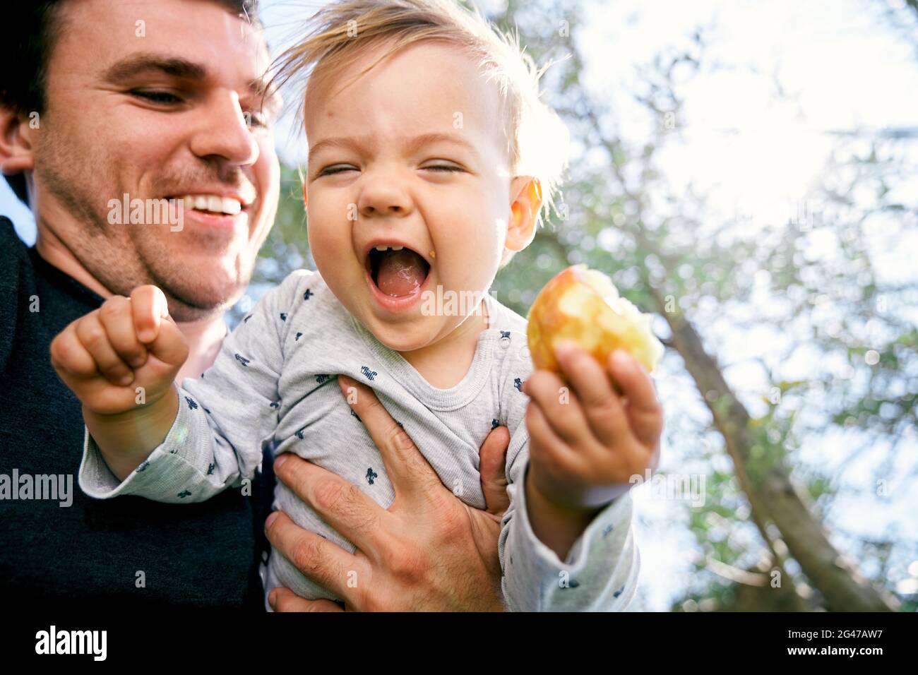Un père souriant tient devant lui un enfant en train de rire avec une poire dans sa main contre un fond de bois. Gros plan. Angle bas Banque D'Images