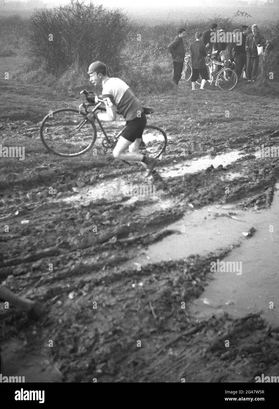 1954, historique, un concurrent qui court avec son vélo dans une course de vélo boueux, Essex, Angleterre, Royaume-Uni. Banque D'Images