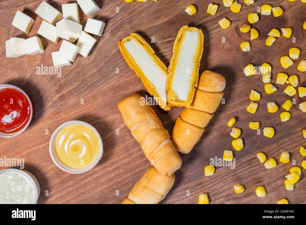 Tequenos au fromage vénézuélien coupé en deux sur fond en bois avec sauces et maïs décortiqué. Banque D'Images