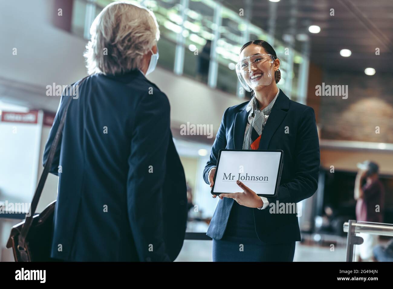 Chauffeur privé portant un masque de protection debout à l'aérogare, tenant une pancarte et recevant un voyageur. Femme chauffeur avec une pancarte à l'aéroport Banque D'Images Chauffeur privé portant un masque de protection debout à l'aérogare, tenant une pancarte et recevant un voyageur. Femme chauffeur avec une pancarte à l'aéroport Banque D'Images