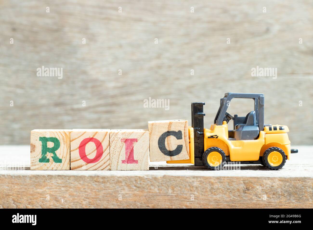 Chariot élévateur à jouets tenir le bloc de lettres c pour compléter le mot ROIC (abréviation de rendement du capital investi) sur fond de bois Banque D'Images