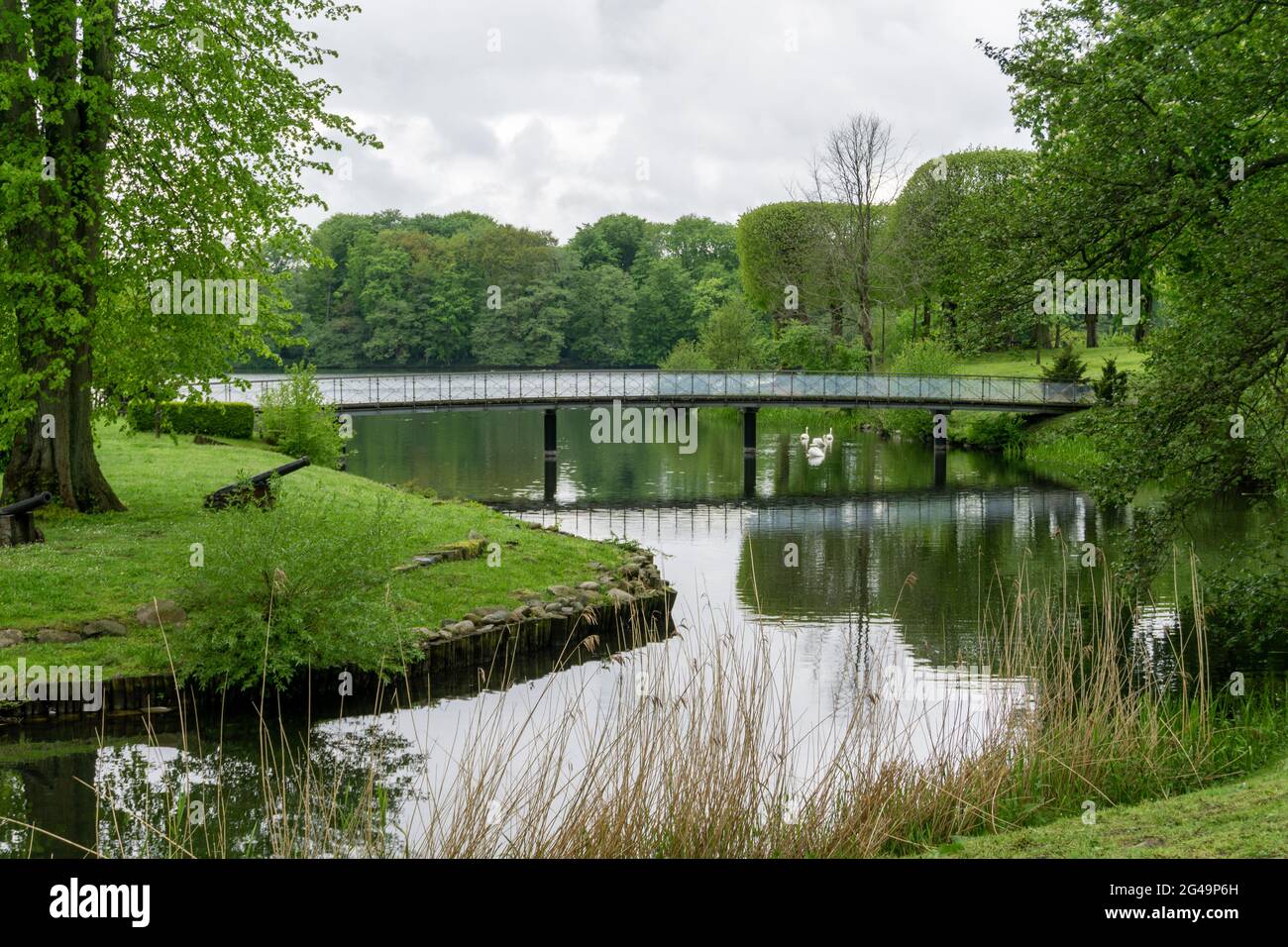 Parc idyllique et paisible à côté d'un étang avec arbres d'été verts et un pont qui traverse Banque D'Images