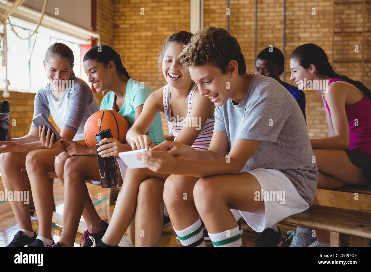 Les enfants de l'école secondaire à l'aide de téléphone mobile tout en vous relaxant dans la région de basket-ball Banque D'Images