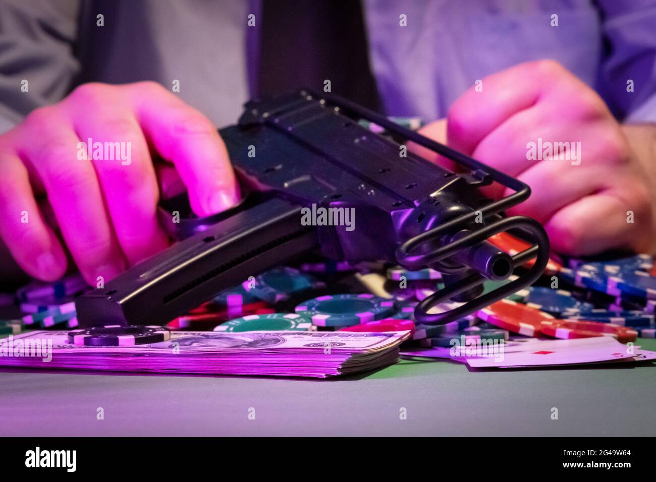 L'homme dans le casino. Il tient une arme dans sa main. Sur la table sont des jetons, de l'argent et des cartes. L'arrière-plan est très flou. Banque D'Images