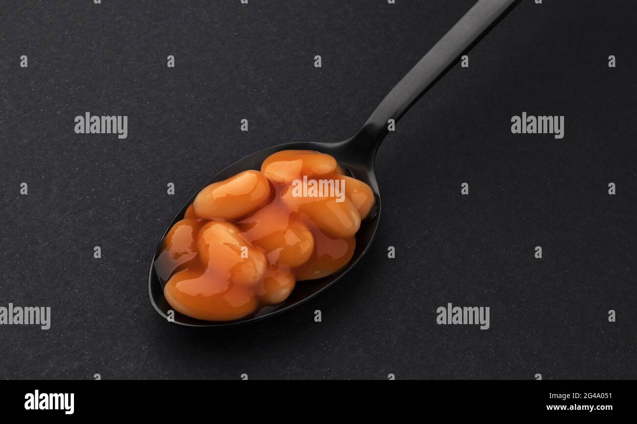 Cuillère de haricots cuits dans la sauce tomate isolée sur fond noir Banque D'Images
