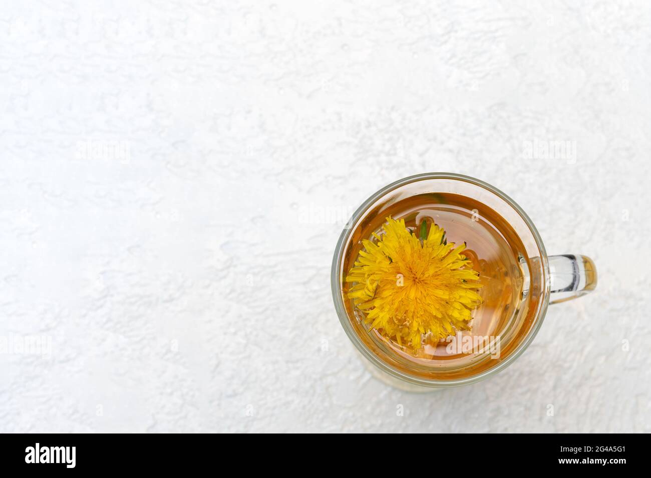 Thé de pissenlit à base de plantes saines dans une tasse de verre et fleur de pissenlit jaune à l'intérieur sur un fond blanc, vue du dessus, espace de copie. Boisson rafraîchissante d'été, t Banque D'Images