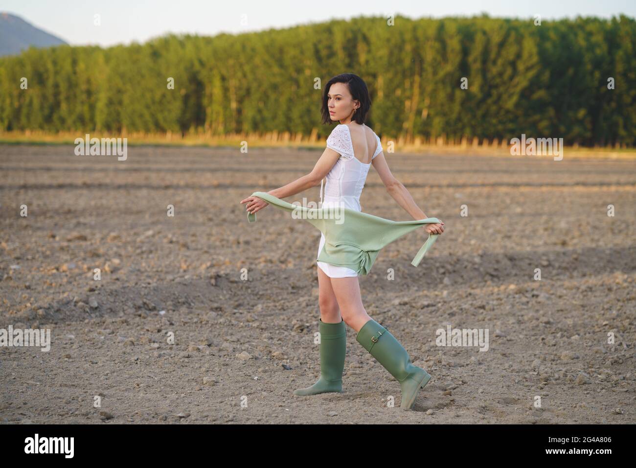 Femme asiatique, marchant dans la campagne, portant une robe blanche et des bottes vertes. Banque D'Images