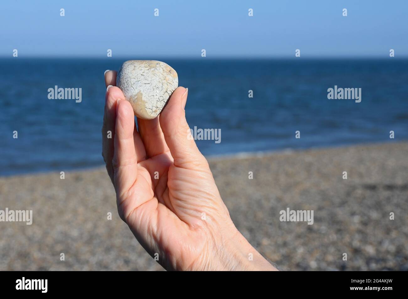 Gros plan d'une femme âgée tenant un galet en forme de cœur. Plage d'Aldeburgh, Aldeburgh, Suffolk, Royaume-Uni Banque D'Images