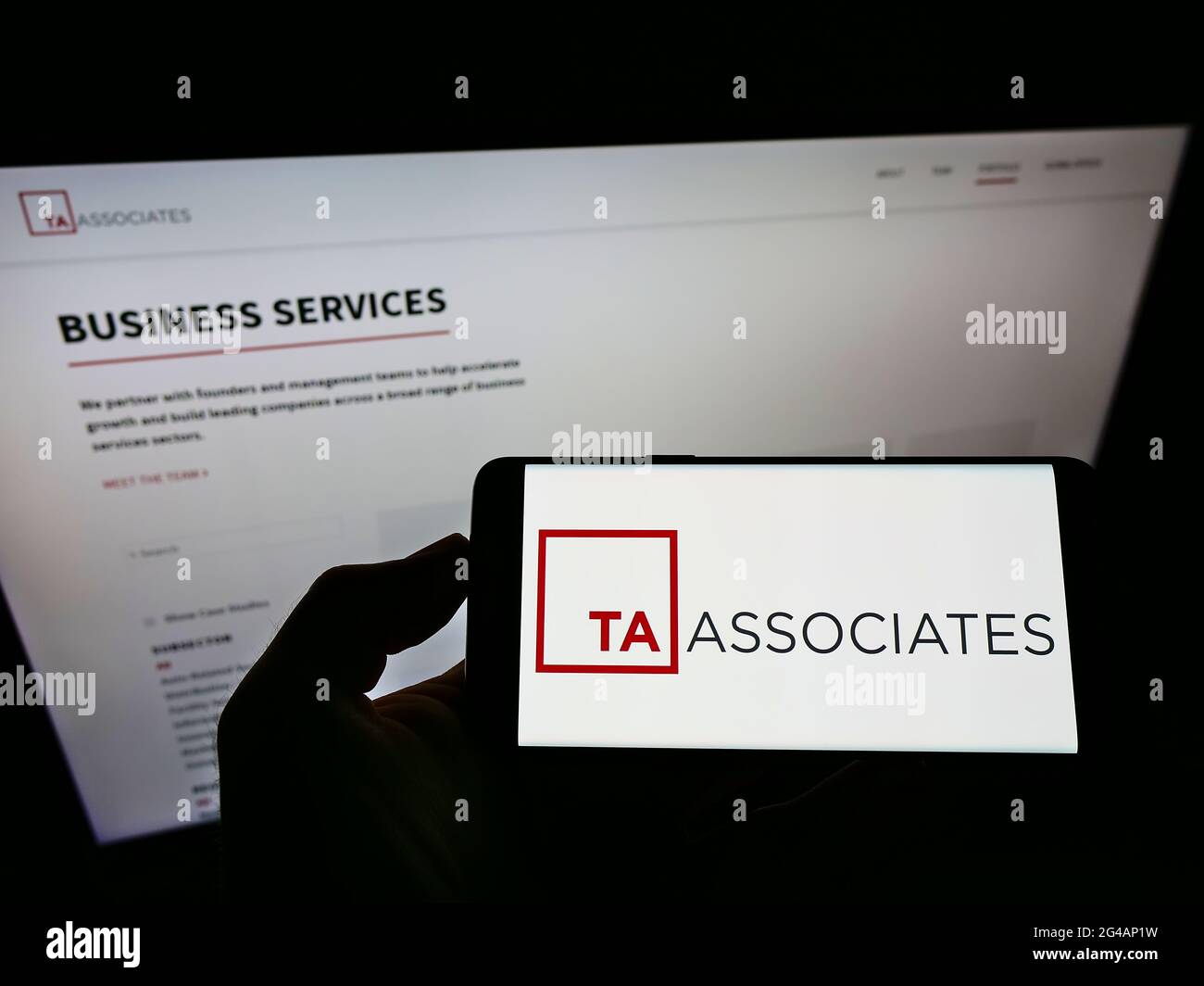 Personne détenant un téléphone portable avec le logo de la société de capital-investissement US TA Associates Management L.P. à l'écran en face de la page Web. Mise au point sur l'affichage du téléphone. Banque D'Images