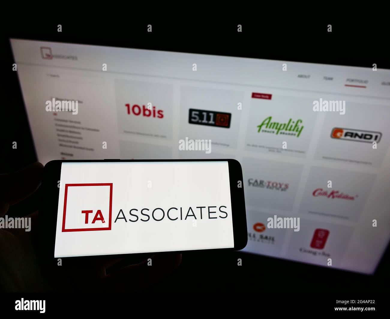 Personne détenant un téléphone portable avec le logo de la société de capital-investissement US TA Associates Management L.P. à l'écran devant la page Web. Mise au point sur l'affichage du téléphone. Banque D'Images