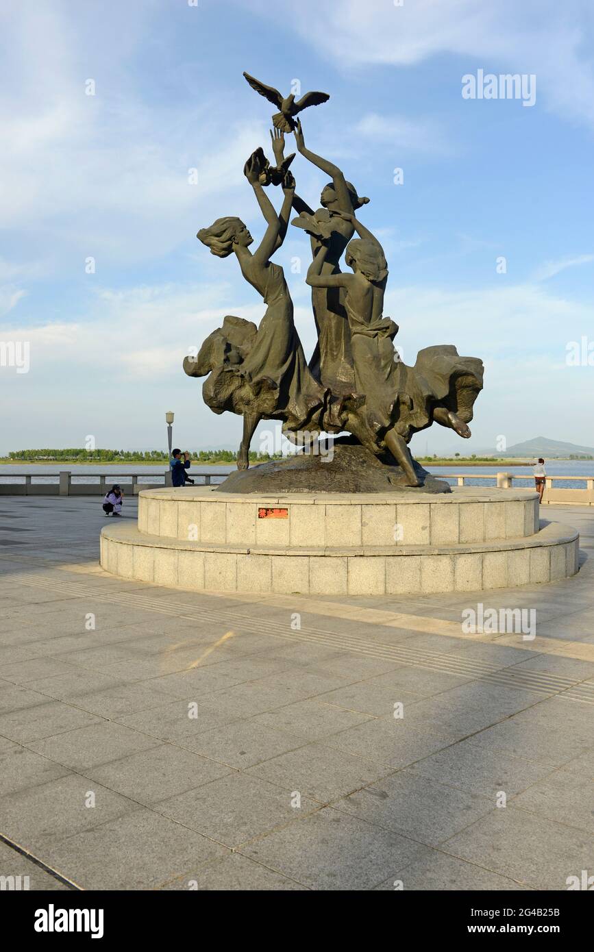 Une statue de personnes libérant des colombes pour la paix se trouve sur le front de mer de la rive nord du fleuve Yalu à Dandong, en Chine, avec la Corée du Nord au-delà Banque D'Images