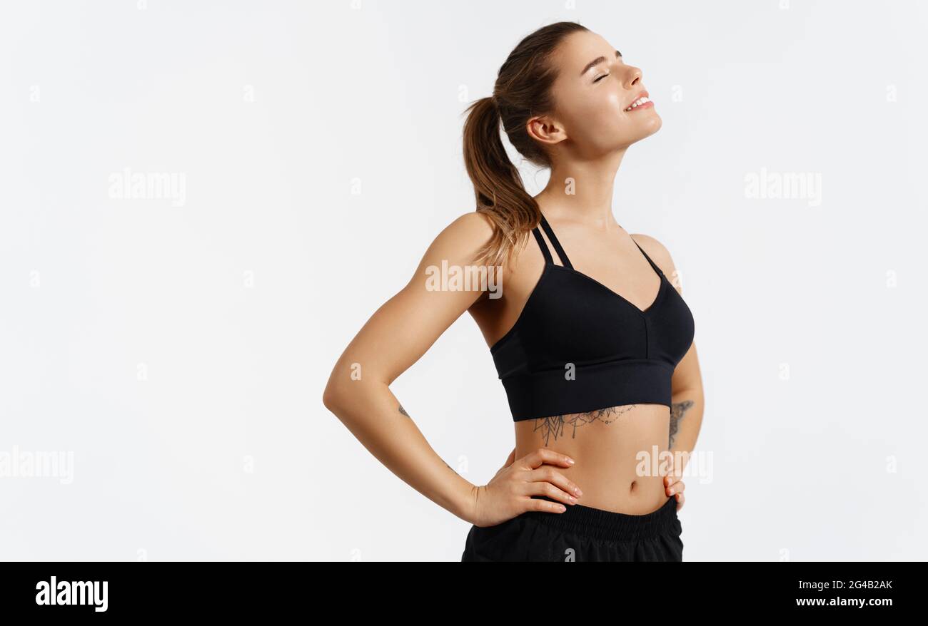 Portrait de la femme en forme dans l'humeur gaie debout satisfait avec les hanches sur le corps, blanc isolé arrière-plan. Une athlète féminine souriante se reposant après l'entraînement Banque D'Images