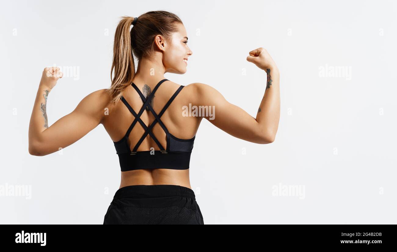 Sport et femmes. Vue arrière d'une athlète de forme physique forte, d'une culturiste féminine, de muscles flexibles, montrant le corps ajusté, les biceps et le dos athlétique, souriant Banque D'Images