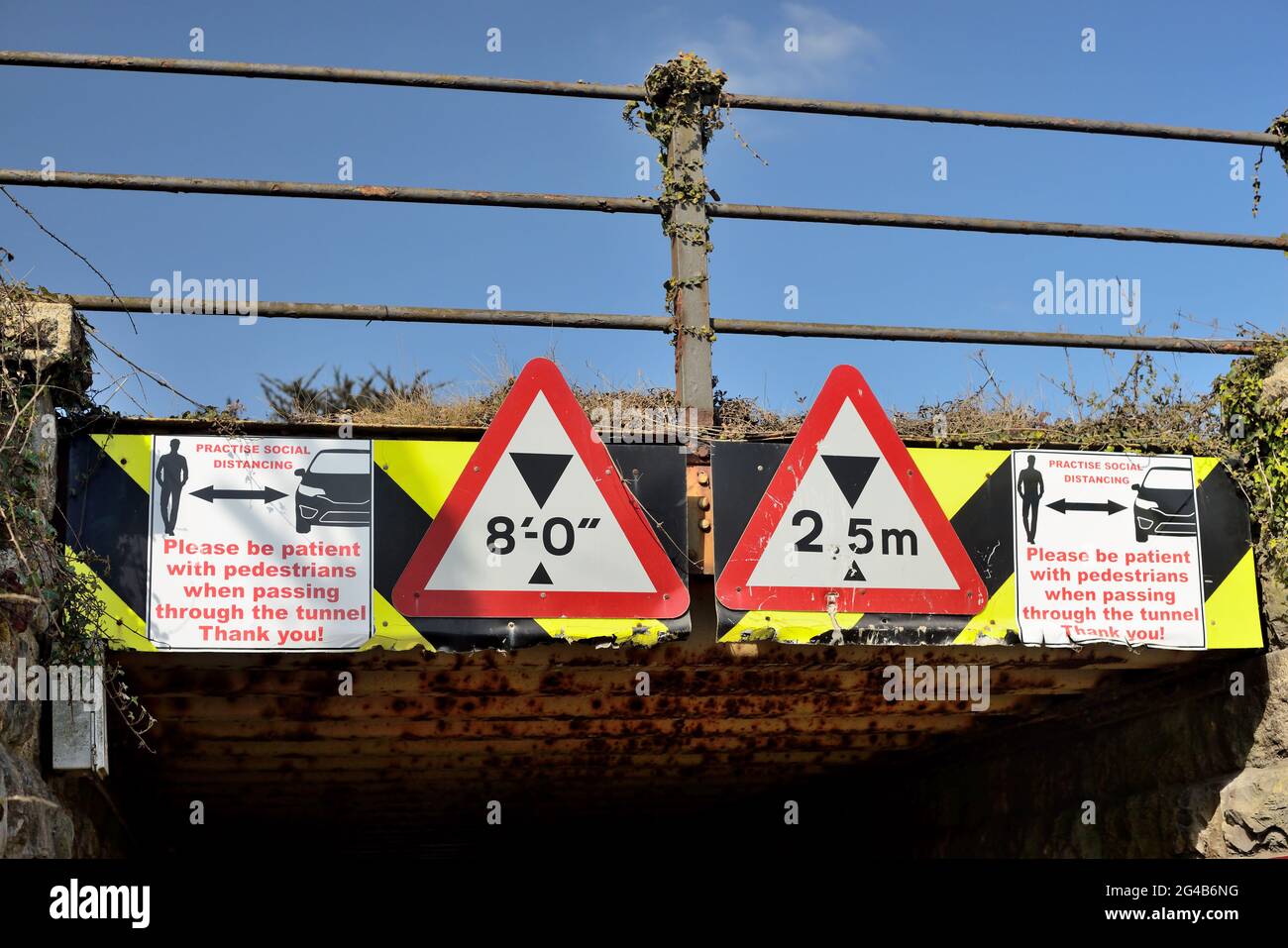 Signes de distanciation sociale sur un pont ferroviaire bas au-dessus d'un tunnel étroit partagé par les piétons et les véhicules à moteur. Banque D'Images